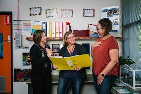 Three educators with yellow folder having discussion