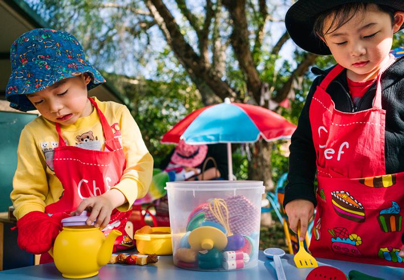 Two children outside wearing hats and playing with kitchen toys