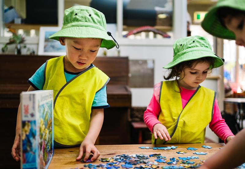 Two children in high-vis vests working on a puzzle together